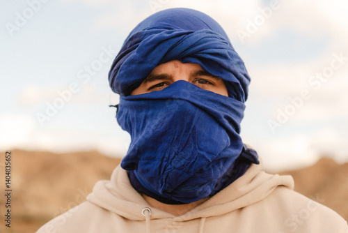 Tourist wearing blue turban and beige hoodie in desert landscape