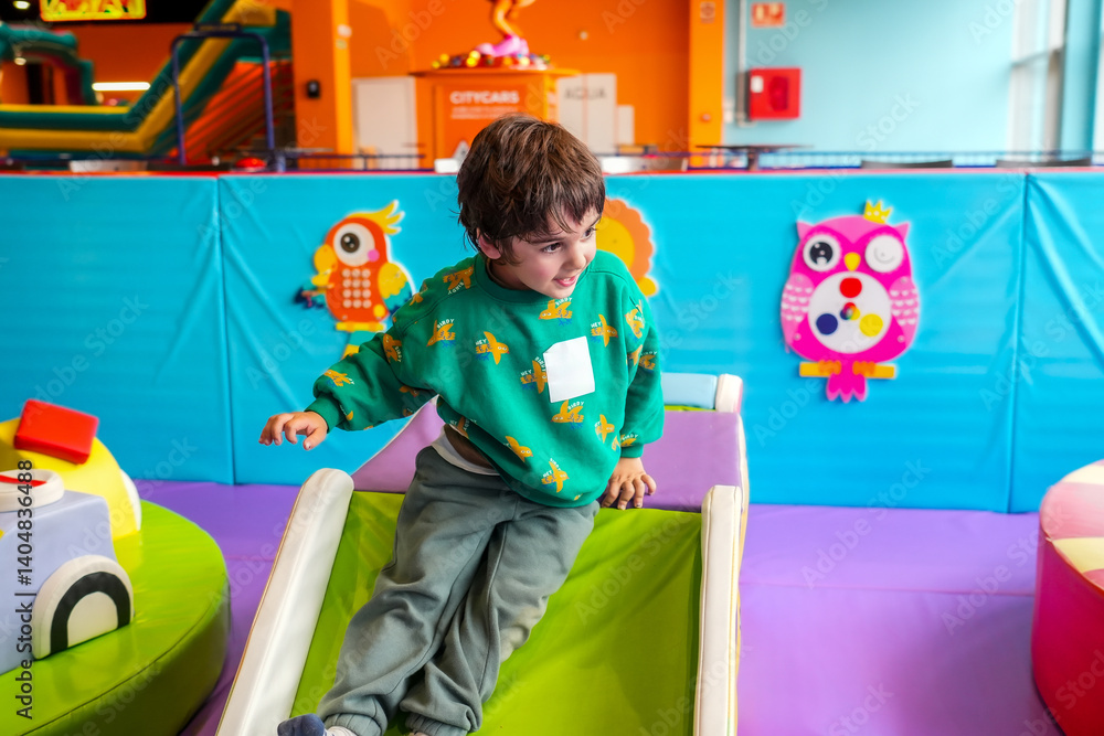 Preschooler boy sliding down at indoor playground