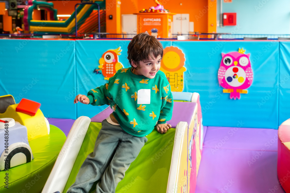 Happy child sliding down in soft play area at indoor playground