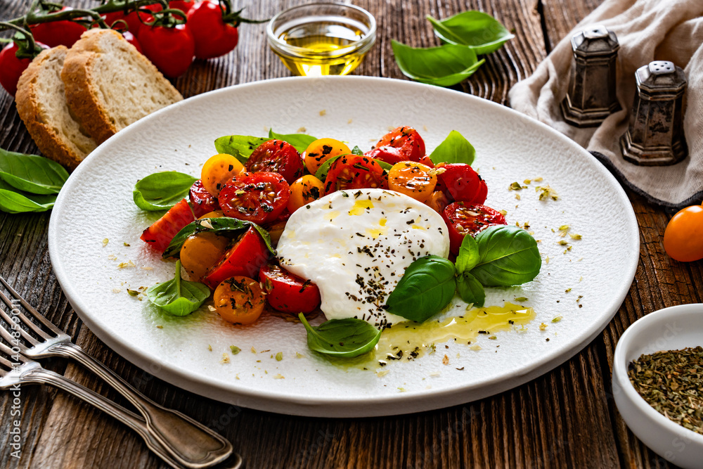 Caprese salad - tomatoes, fresh basil leaves and burrata cheese on wooden background