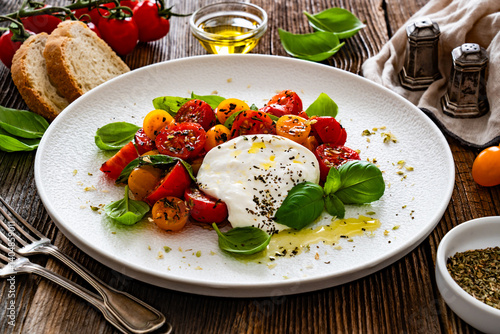 Obraz na płótnie Caprese salad - tomatoes, fresh basil leaves and burrata cheese on wooden background w salonie