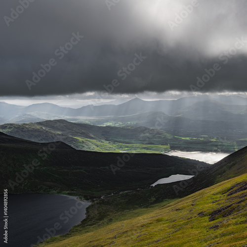 Wallpaper Mural Dark, brooding clouds above a green, hilly landscape.  Light breaks through, illuminating parts of the scene. Torontodigital.ca