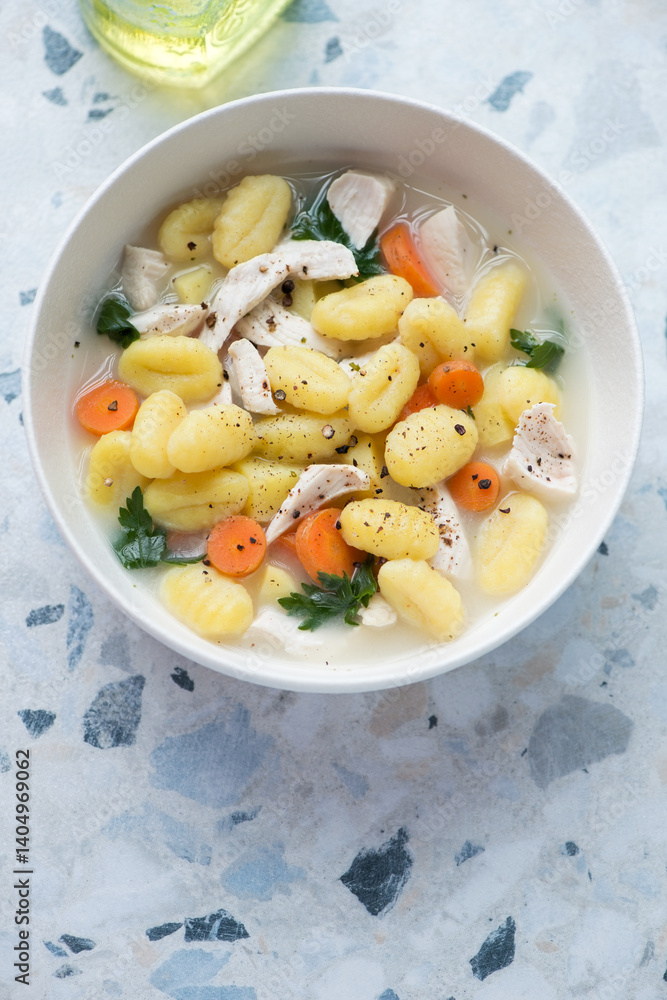 Bowl of chicken soup with potato gnocchi on a white and blue granite background, vertical shot, high angle view Bowl of chicken soup with potato gnocchi on a white and blue granite background, vertical shot, high angle view