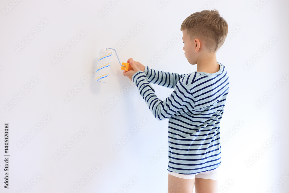 A young boy renovating a room, sanding the walls with sandpaper and painting them white with a roller. Home improvement and DIY repair concept A young boy renovating a room, sanding the walls with sandpaper and painting them white with a roller. Home improvement and DIY repair concept
