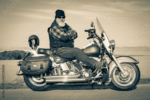 Kräftig gebauter Rocker sitzt auf einem klassischen, schweren Motorrad am Straßenrand, Sepia - Aufnahme.sepia.