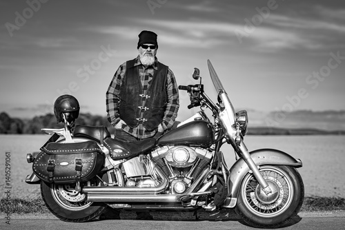Rocker mit einem kultigen Motorrad possiert auf einer Landstraße, schwarz-weiß Aufnahme.