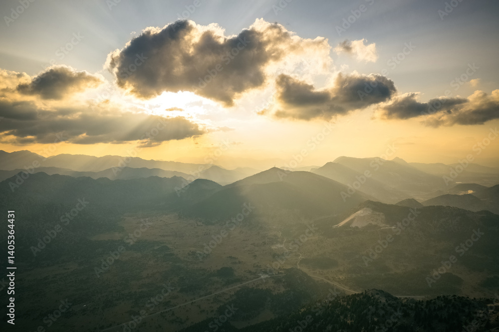 Dramatic sky with yellow sun rays streaming through the clouds onto the mountains at sunrise in the early morning.