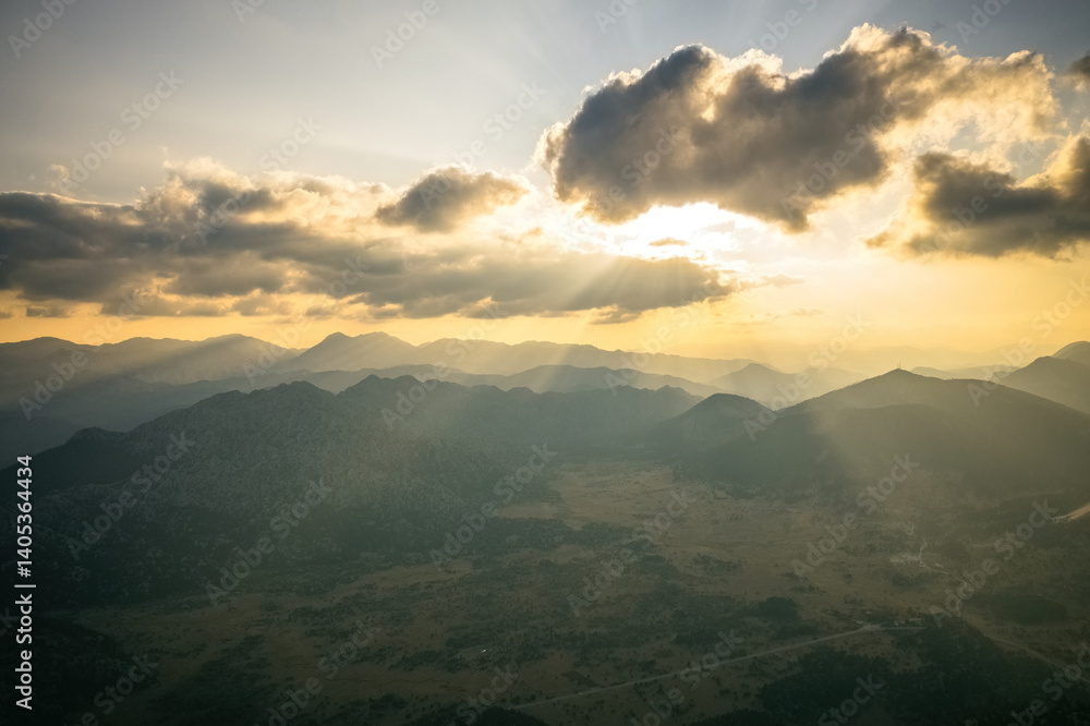 Dramatic sky with yellow sun rays streaming through the clouds onto the mountains at sunrise in the early morning.
