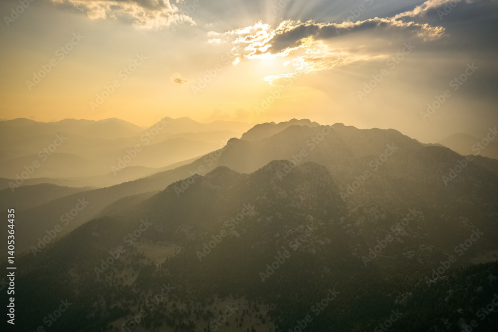 Dramatic sky with early morning sunrise with sun rays penetrating through the clouds onto the mountains.