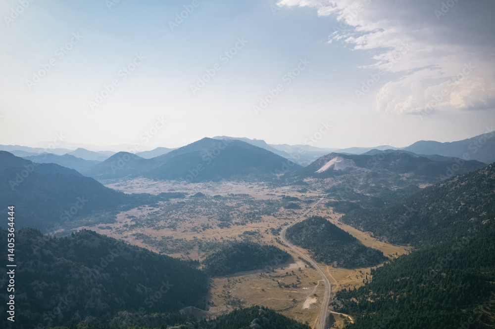 Magnificent nature photo taken with drone footage. An asphalt road passes through the middle of the mountainous and forested valley.