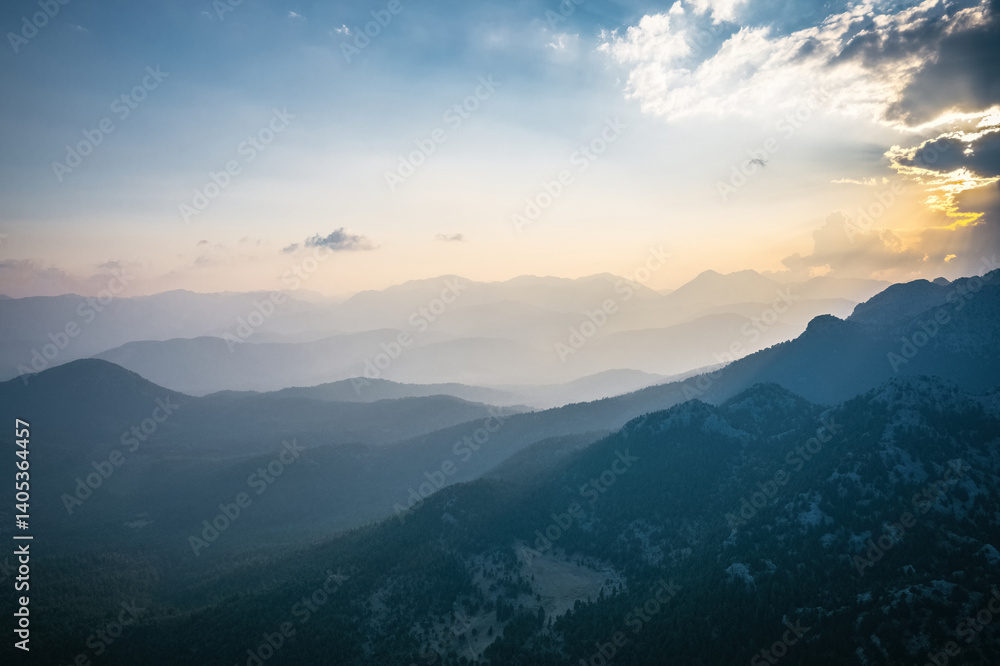 An impressive sunrise skyscape in the early morning. Yellow sun rays filter through the clouds towards the mountains and the ground.