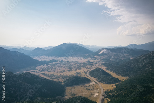 Magnificent nature photo taken with drone footage. An asphalt road passes through the middle of the mountainous and forested valley.
