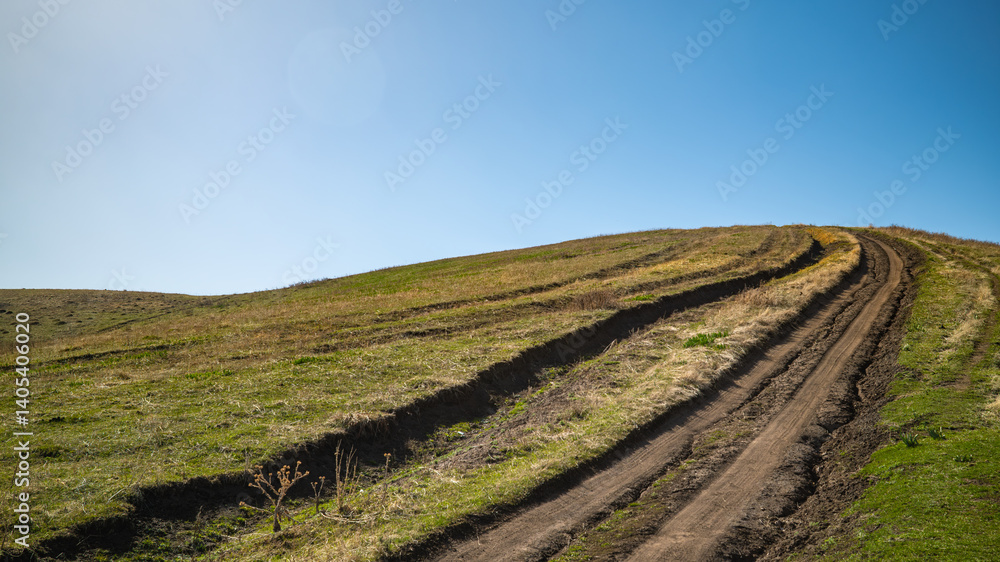 Dirt road winding uphill through green meadow under clear blue sky Dirt road winding uphill through green meadow under clear blue sky