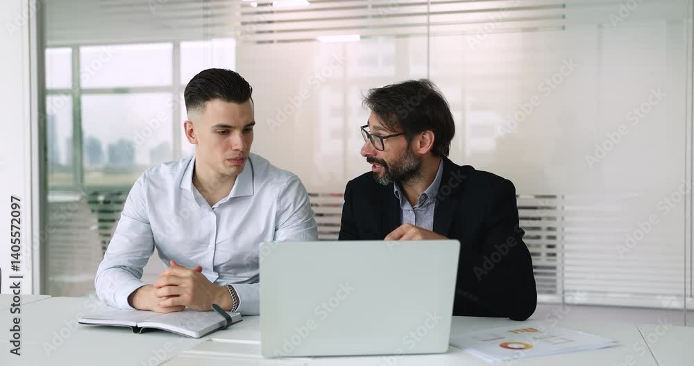 Two men engaged in formal conversation, contributing to collaborative work seated at table with laptop during meeting. Mentorship, strategic planning, decision-making and teamwork using modern tech Two men engaged in formal conversation, contributing to collaborative work seated at table with laptop during meeting. Mentorship, strategic planning, decision-making and teamwork using modern tech