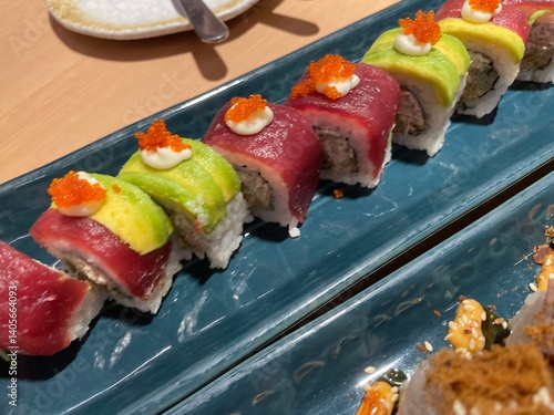 A close-up, top-down view showcases two rows of beautifully crafted sushi rolls on a textured blue plate.