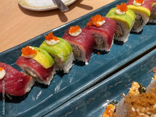 A close-up, top-down view showcases two rows of beautifully crafted sushi rolls on a textured blue plate.