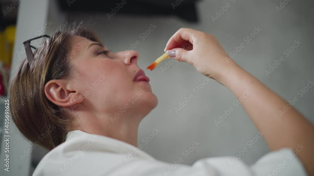 Playful woman wearing white top raises head slightly while eating chips dipped in sauce indoors with blurred background visible showing relaxed casual moment during break in cozy home Playful woman wearing white top raises head slightly while eating chips dipped in sauce indoors with blurred background visible showing relaxed casual moment during break in cozy home