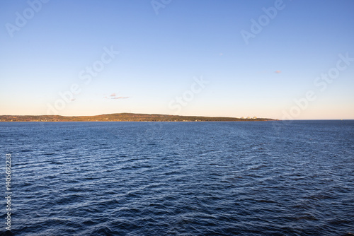 Photograph of Calm rippling ocean water surface land on the horizon on bright blue sunny morning.