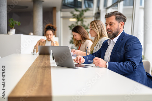 Male professional holding glasses and using laptop while female colleagues working together in meeting