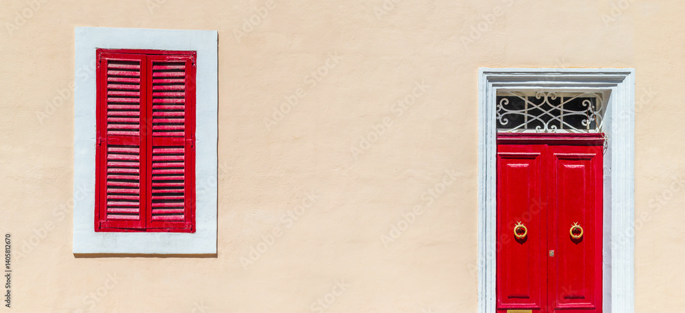House facade colored in warm beige pastel color with bright red door and shuttered window