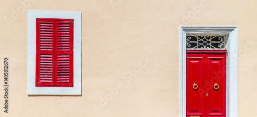 House facade colored in warm beige pastel color with bright red door and shuttered window