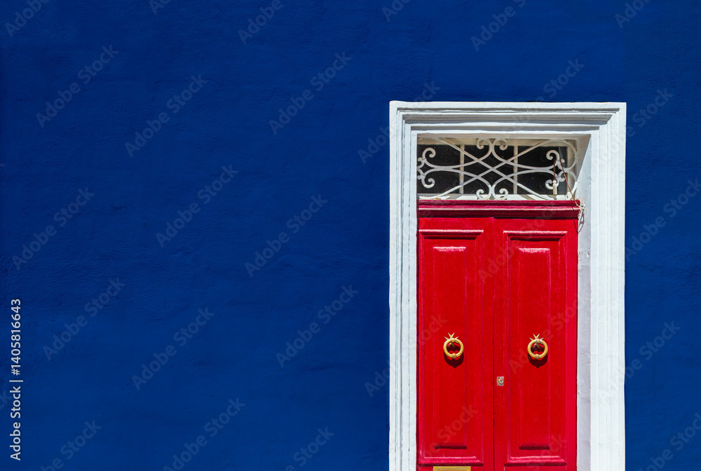 High contrast photograph of dark blue wall of residential building facade with red door