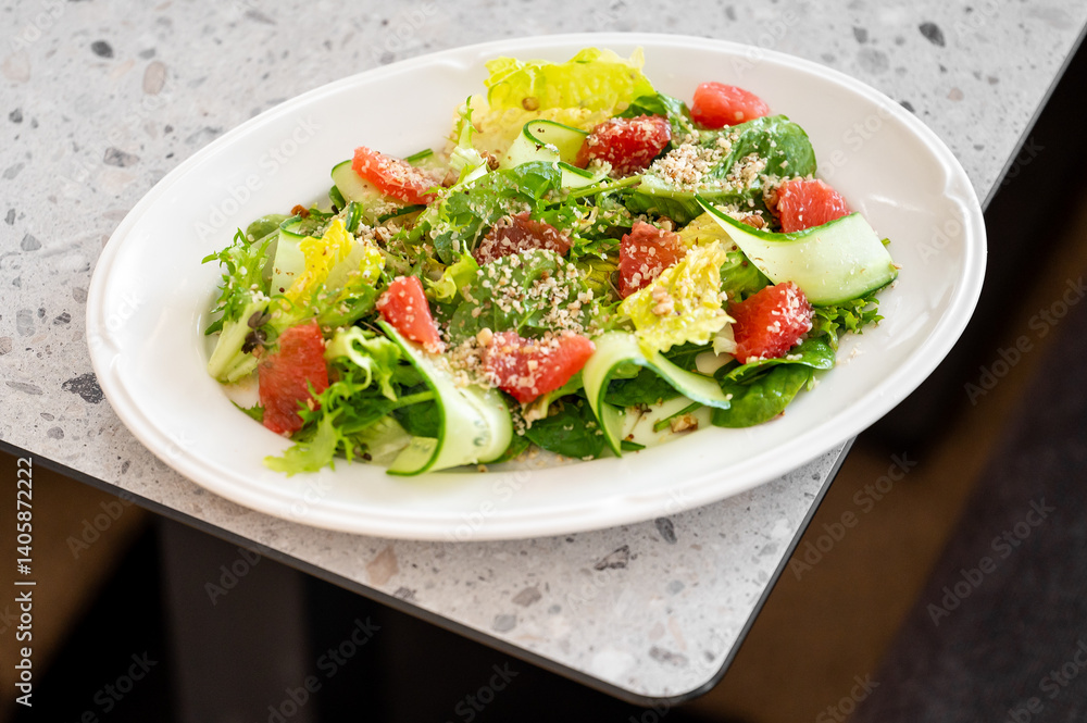 A colorful salad featuring fresh greens, cucumbers, and diced tomatoes is served on an oval white plate. The vibrant ingredients highlight a healthy dining choice on a textured surface. A colorful salad featuring fresh greens, cucumbers, and diced tomatoes is served on an oval white plate. The vibrant ingredients highlight a healthy dining choice on a textured surface.
