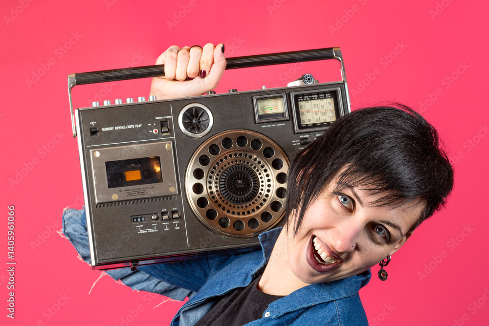 Beautiful gothic style brunette young woman with retro vintage tape cassette recorder against pink red background