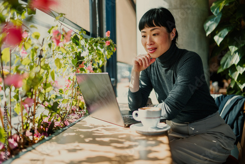 Asian freelancer working on laptop in cafe with plants
