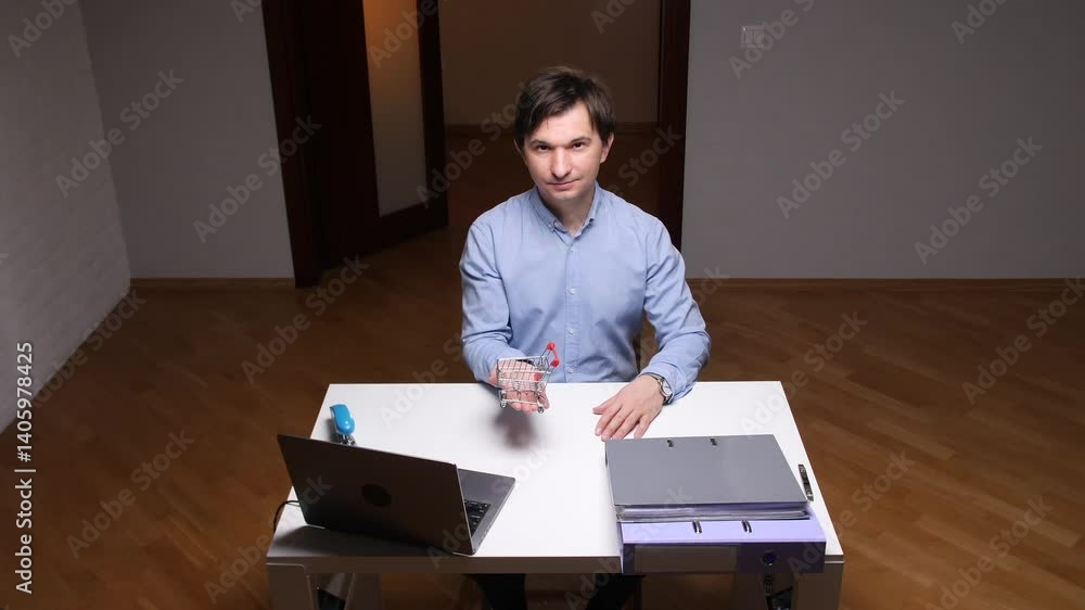 Office worker showing shopping cart at desk with laptop and folders Office worker showing shopping cart at desk with laptop and folders