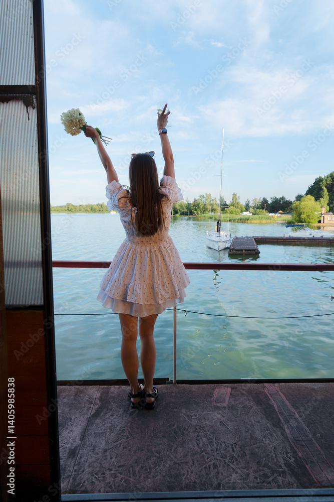 Fototapeta premium A joyful woman is celebrating by the peaceful water, holding vibrant flowers and enjoying the beautiful view around her
