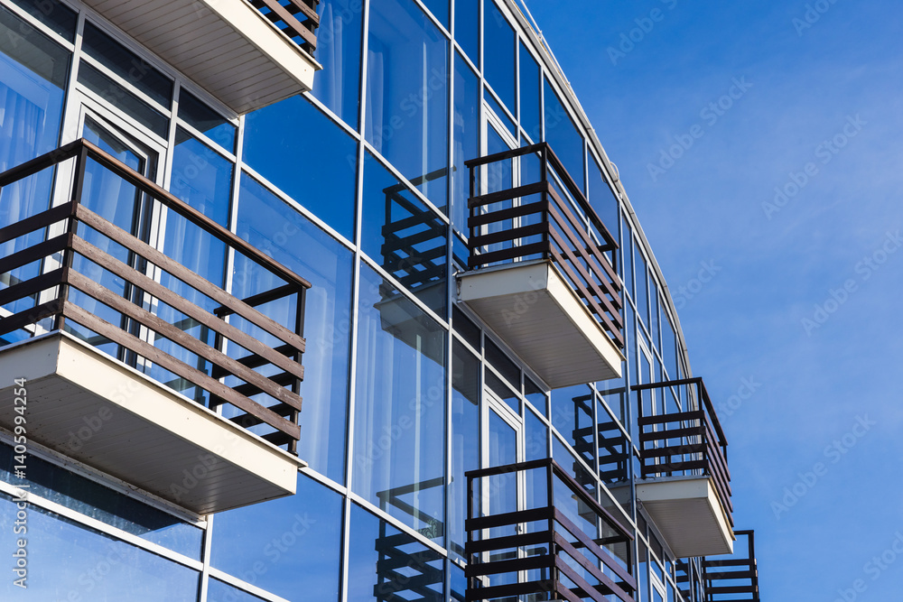Elegant glass building featuring wooden balconies, reflecting the sky