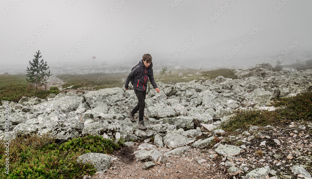 Obraz premium A boy explores the rugged landscape of Dalarna, Sweden, navigating through rocky terrain and green in the mist, enjoying the beauty of nature while hiking