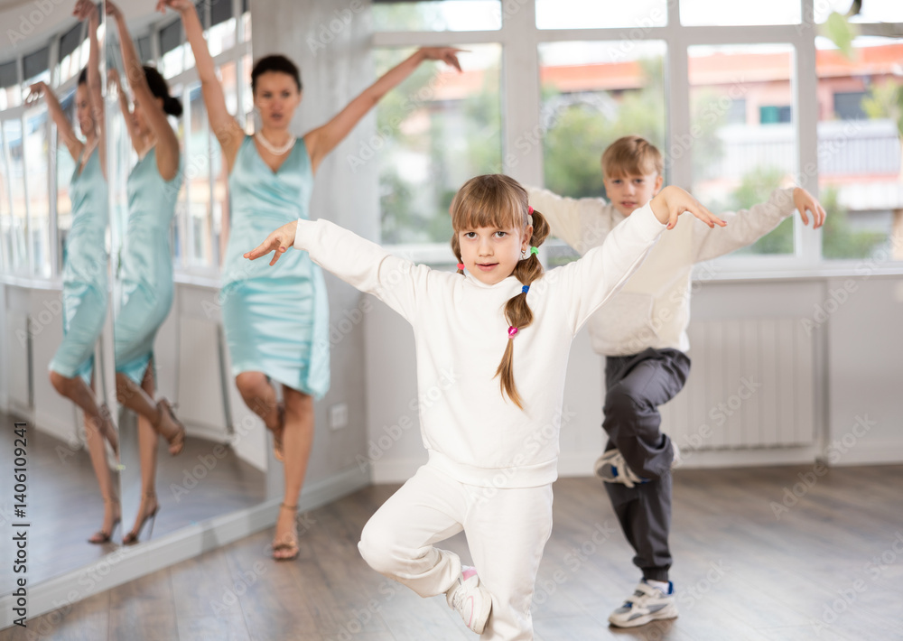 Naklejka premium Boy and girl kids repeat movement while taking hip hop dancing lessons. Female teacher conducts class for students during dance workout and watches performing movements