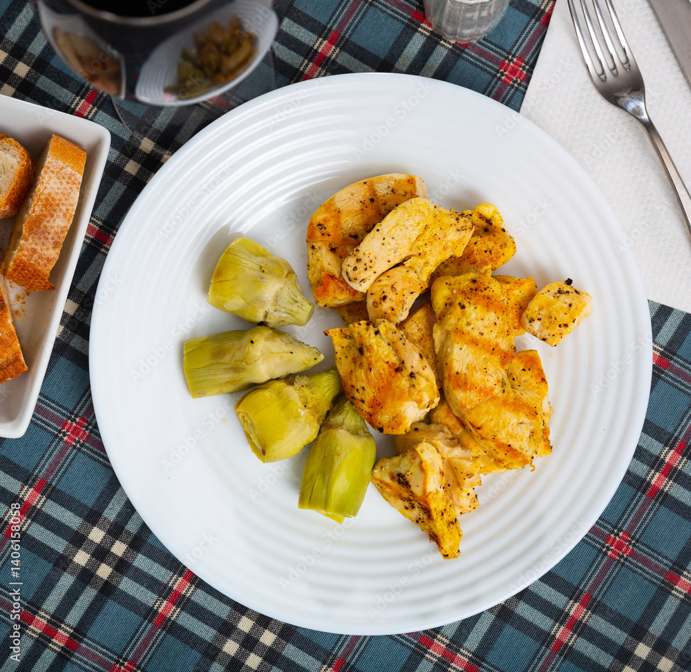 Traditional Spain cuisine, roasted chicken fillet and artichokes on a white plate Traditional Spain cuisine, roasted chicken fillet and artichokes on a white plate