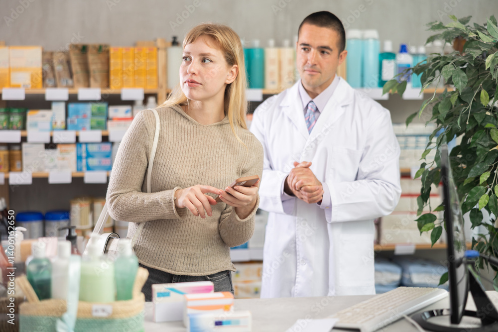 Obraz premium Woman scrolls through online catalog on the pharmacy website against the background of a pharmacist. Customer holds a mobile phone in hands in a pharmacy and looking at shelves with goods