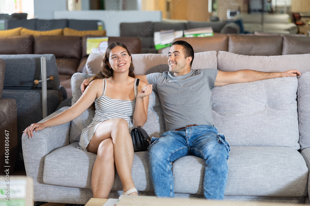 In furniture store,girl is sitting on couch.She leaned comfortably on back of sofa to make sure comfort of chosen model.Girl and husband pick up light sofa for living room in new apartment