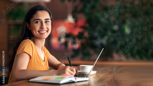 Obraz na plátně Female student looking for part-time job, taking notes and using laptop at cafeteria, free space
