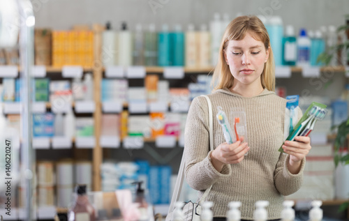 Attentive young woman holding toothbrush trying to make choice in chemist's shop
