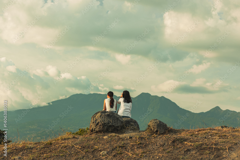 Obraz premium two people sitting on a rock, facing the mountain
