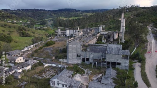 Aerial Drone Flight Over a Ghost Town in Colombia. Haunting aerial footage of a ghost town in Colombia, where abandoned buildings with gray facades and roofs stand in contrast to the dense forest near