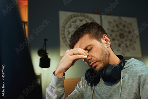 Obraz na płótnie Tired man rubs eyes while working at computer. Fatigued freelancer working late at home office. Concept of stress and mental fatigue during remote work w salonie