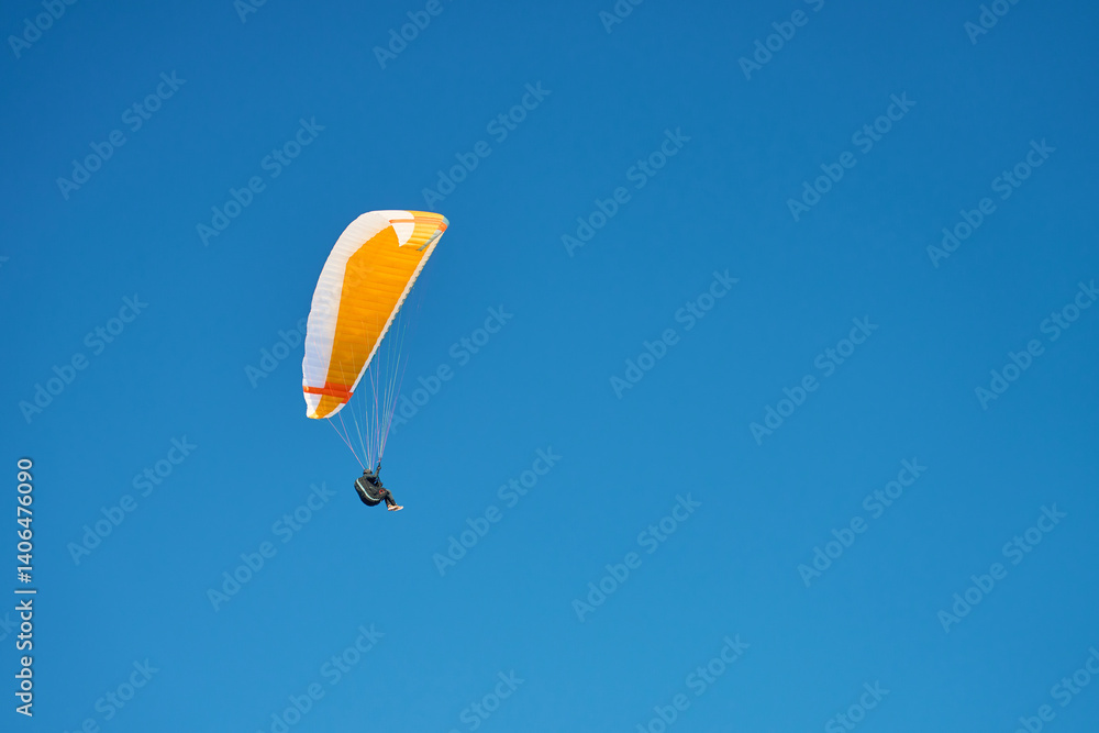 Person is flying on paraglider against blue sky. Paraglide with yellow canopy. Extremal sport