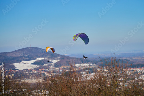 Obraz na płótnie Two paragliders fly above snowy landscape with mountains and town on clear day. Concept of freedom, adventure, and outdoor sports w salonie