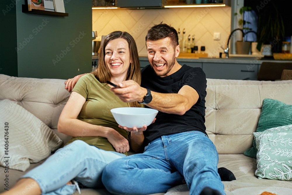 Man and woman enjoying evening together in living room. Couple sitting on couch watching TV, holding remote and snack bowl. Concept of entertainment and spending time together