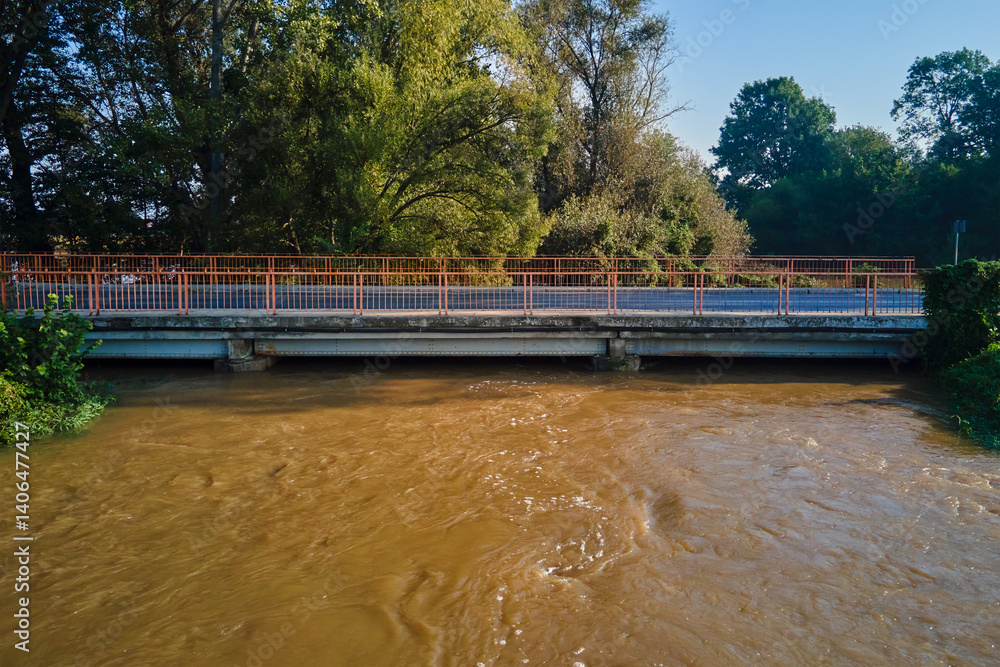 Brown muddy water flows under road bridge. Flooded river after heavy rainfall. Natural disaster