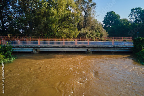 Obraz na płótnie Brown muddy water flows under road bridge. Flooded river after heavy rainfall. Natural disaster w salonie