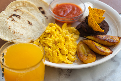 Close-up of a traditional Guatemalan breakfast of fried eggs, beans with nachos, sour cream, fried plantains, orange juice, and tortillas