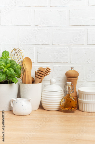 Kitchen utensils, basil plant and condiments resting on wooden countertop in front of white brick wall