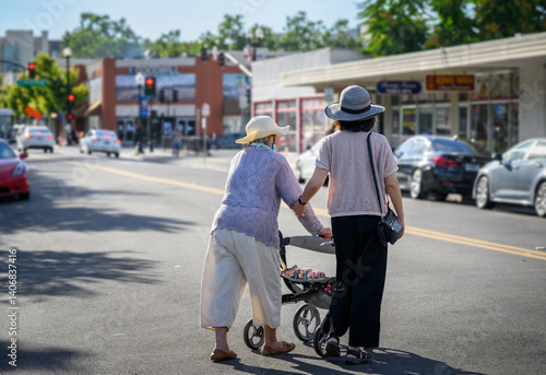 Senior woman walking using a mobility walker, crossing the street with the help of adult daughter. California.